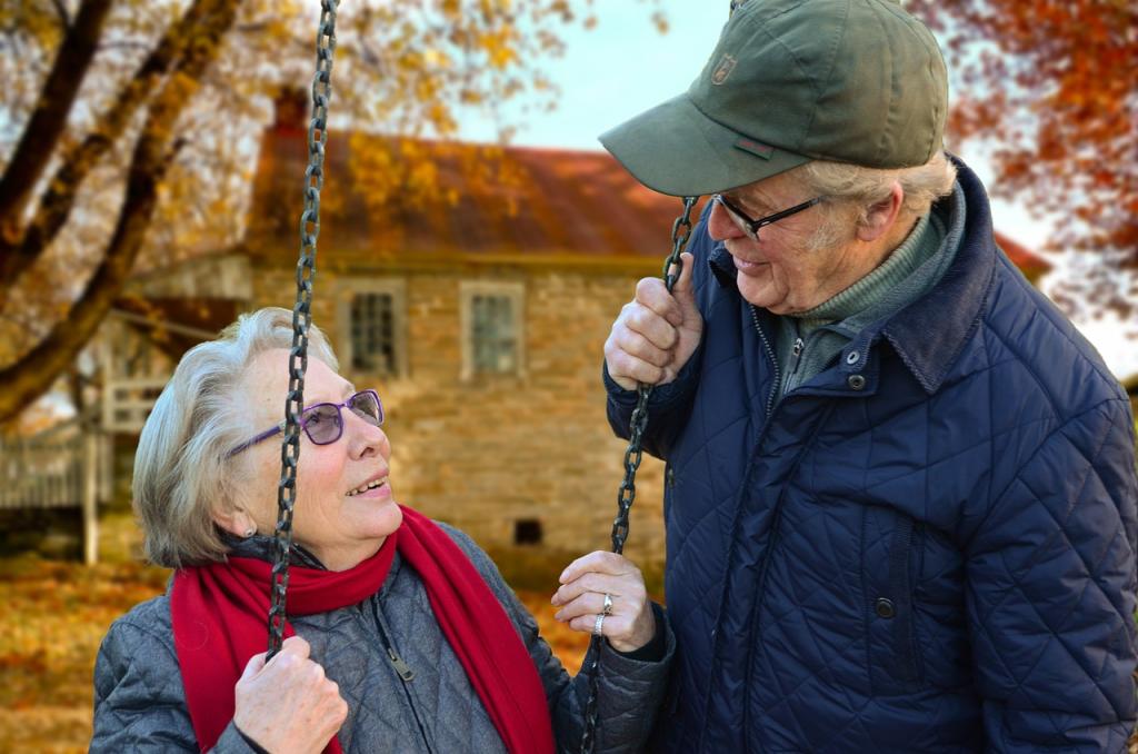 Kaksi senioria ulkoilemassa syksyisessä maisemassa; nainen istuu kiikussa ja mies seisoo hänen vierellään.