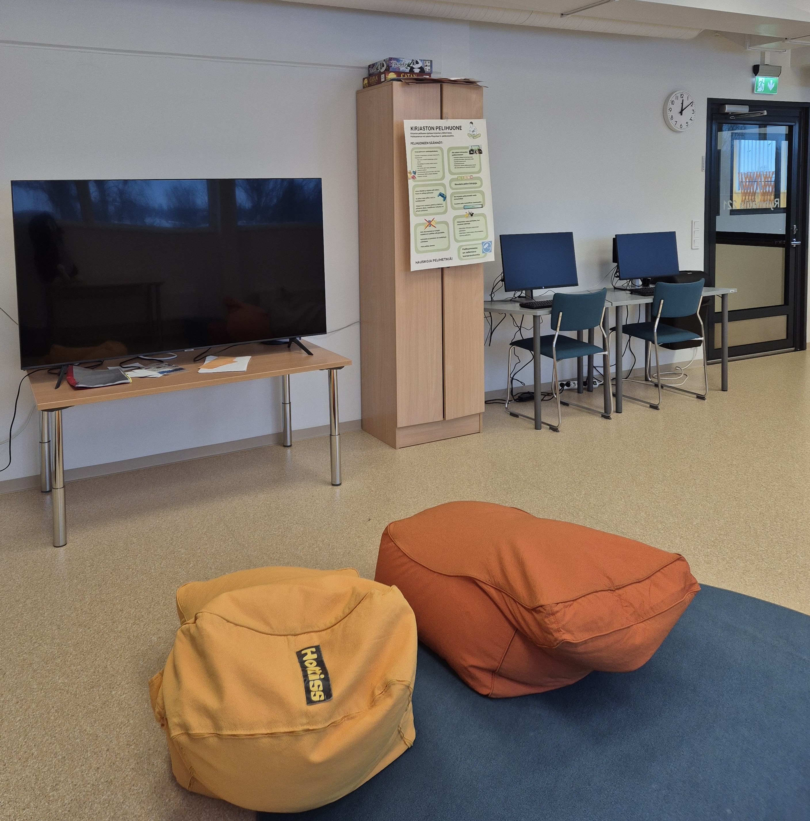 Pelitilassa on iso näyttö, jonka edessä on kaksi säkkituolia, sekä kaappi ja kaksi tietokonetta. 