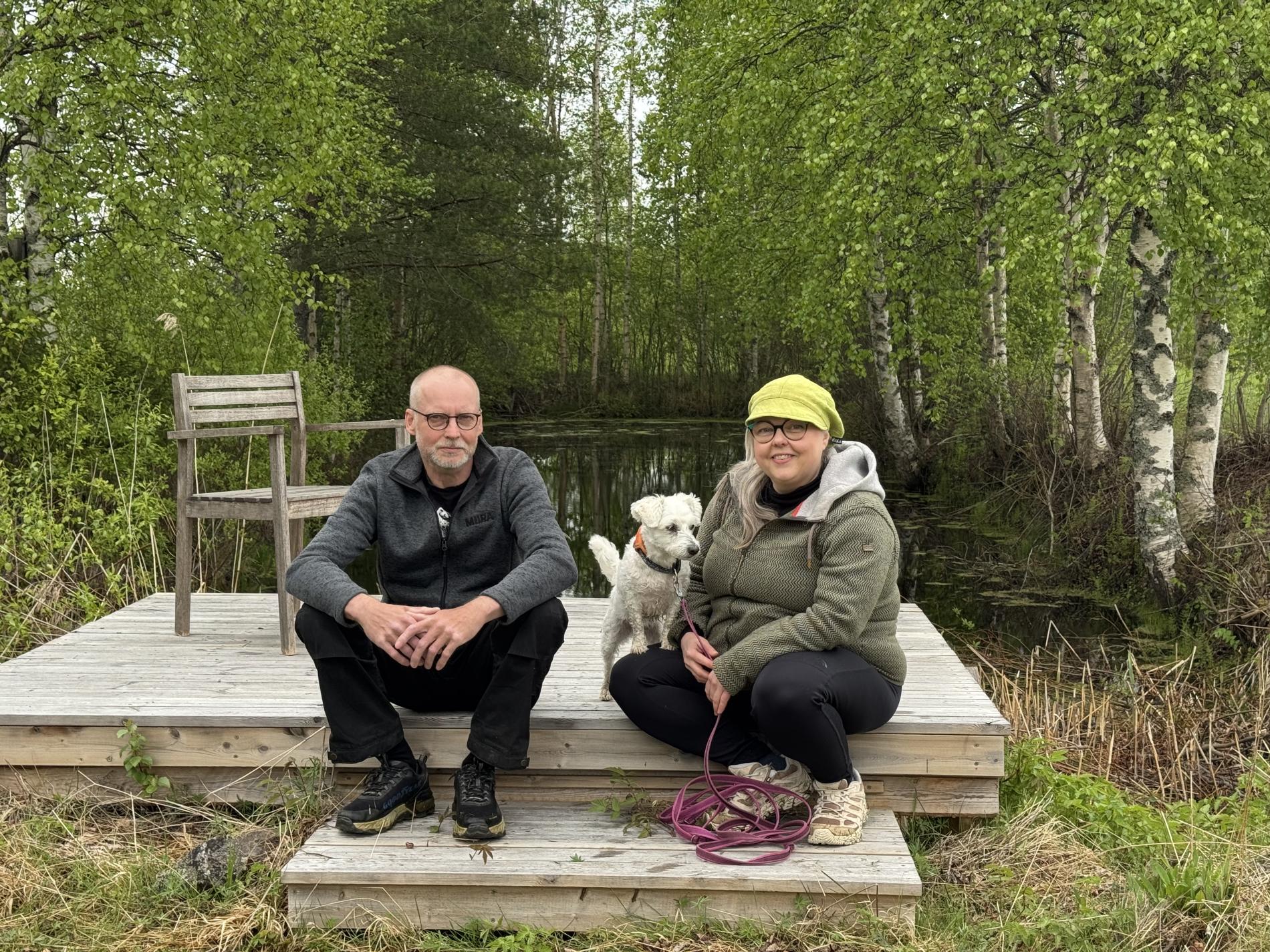 Jarkko, Päivi ja Essi-koira koivujen ympäröivän lammen edustalla.