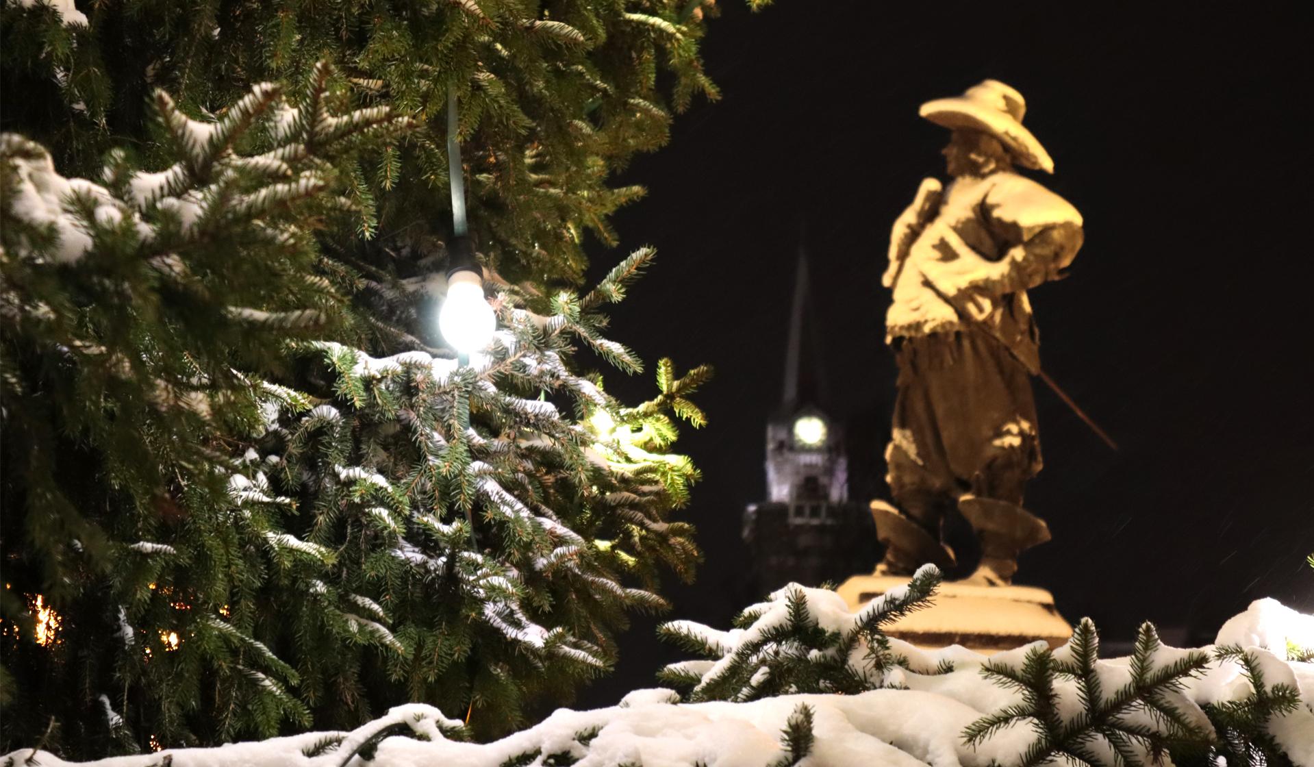 Den snötäckta Pekka-statyn fotograferad med granens grenar.