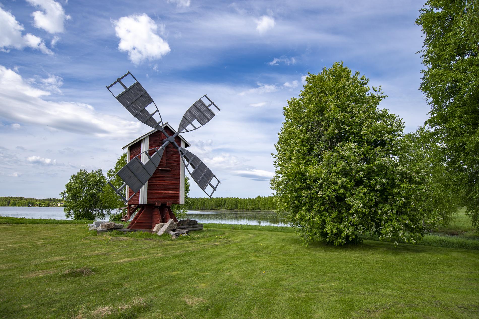 A wooden windmill on the shore of the summer-green Lake Kirkkojärvi.