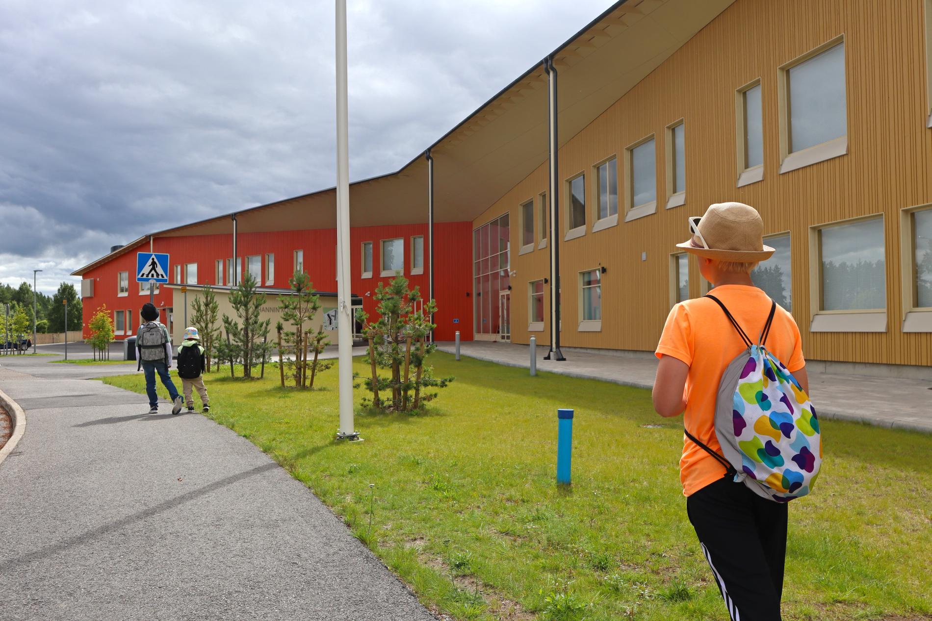 Three children with backpacks in front of the newly built school centre.
